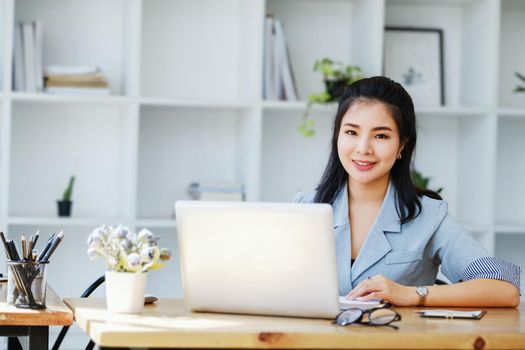 An Asian entrepreneur or businesswoman shows a smiling face while working with using computer on a wooden table