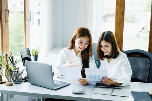 Consulting, learning, marketing, investment, finance, data analysis, research, two Asian women smiling and holding papers, sitting and analyzing financial statements and using computers at work