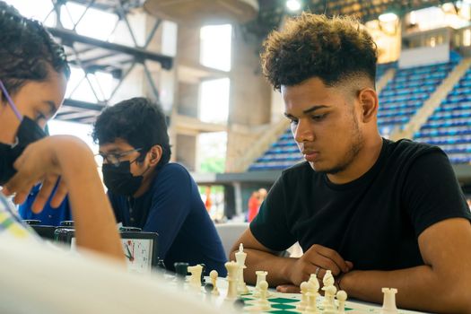 Young Latin man thinking about his move during a chess game in a gym. Concept of intelligence and strategy in the youth of Latin America.