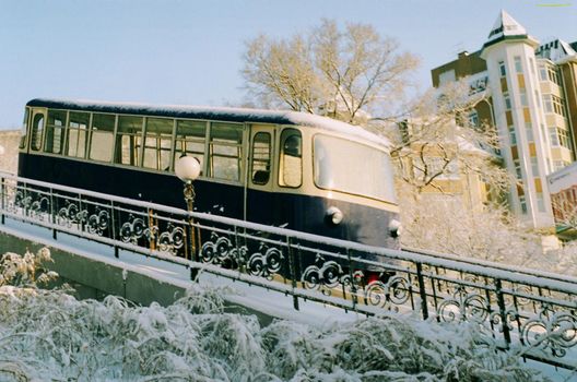 A black tram descends a mountain against the backdrop of snow-covered grass and architecture. The funicular rides up the mountain. Russia. Vladivostok.