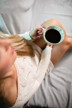 Cup of hot morning coffee held by woman. Sexy female legs with light skin complexion. Relaxing in the comfort of home.