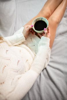 View from above as a woman with slim legs holds a porcelain cup with her morning coffee in her hands. Love coffee and relaxing in the comfort of home.