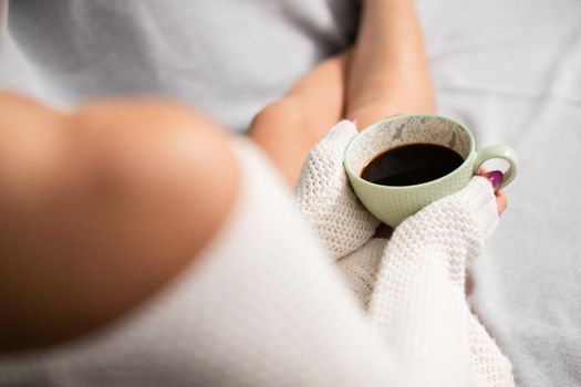Top view of a woman holding a porcelain cup of coffee in her hands. Light complexion of the skin. Love for coffee and relaxation in the comfort of home.