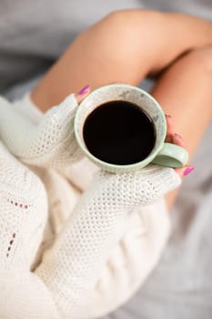 View from above as a woman in a cream sweater holds a delicately porcelain cup with hot coffee. Love coffee and relaxing in the comfort of your home.