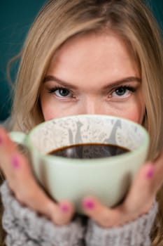 A large cup with hot coffee covers the face of a pretty young woman. Blonde woman during her morning ritual of drinking aromatic coffee.
