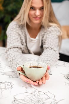 A pretty girl with fair European skin holds a cup full of morning coffee in her hands. A blonde girl shares her morning coffee.