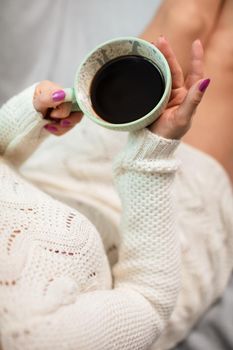 Close-up view of a porcelain coffee cup held by a woman's delicate hands. The love of coffee and relaxation in the comfort of home.