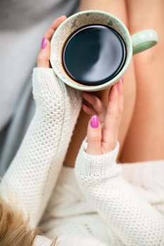 View from above as a woman in a cream sweater holds a delicately porcelain cup with hot coffee. Love coffee and relaxing in the comfort of your home.