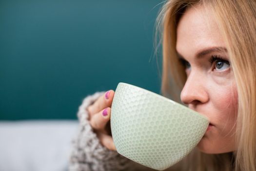 A young woman drinks hot coffee from a large cup in the morning. Close-up view. Aromatic coffee time while resting and relaxing.