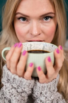 A large cup with hot coffee covers the face of a pretty young woman. Blonde woman during her morning ritual of drinking aromatic coffee.