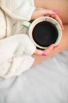 Close-up view of a porcelain coffee cup held by a woman's delicate hands. The love of coffee and relaxation in the comfort of home.