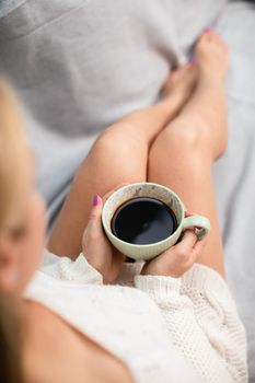 View from above as a woman with slim legs holds a porcelain cup with her morning coffee in her hands. Love coffee and relaxing in the comfort of home.