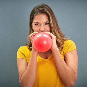 Shot of a young woman inflating a balloon against a gray background.