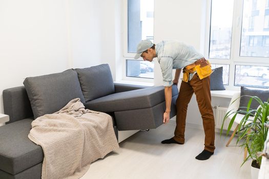 Relocation Concept. Portrait of confident male repairman moving sofa new apartment, replacing furniture at home, caucasian guy placing sofa in cozy studio, side view