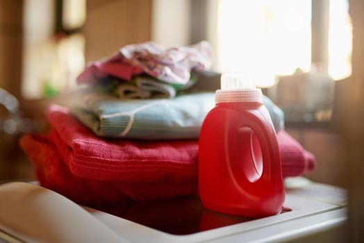 Shot of a bottle of detergent and a pile of laundry on top of a washing machine.