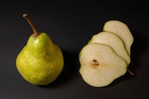 Two ripe green pears on a dark background, late november pear variety. Whole pear and sliced