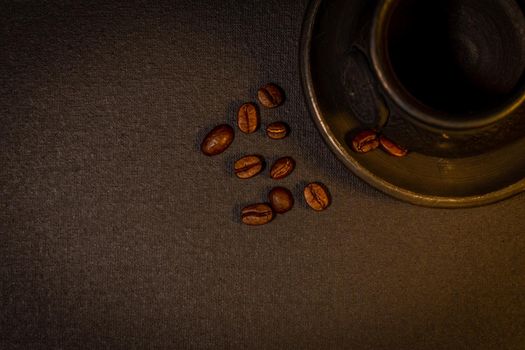 Black clay coffee cup with a saucer and scattered coffee beans near it on dark background