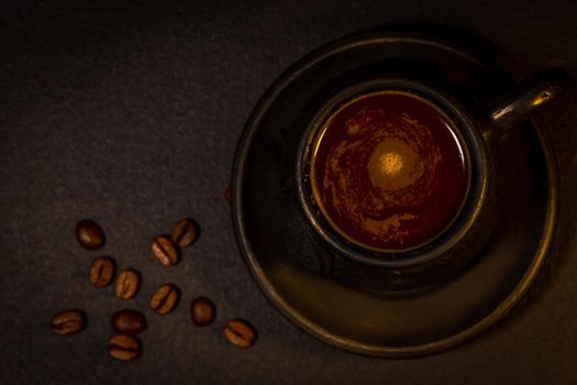 Black clay coffee cup with a saucer and scattered coffee beans near it on dark background