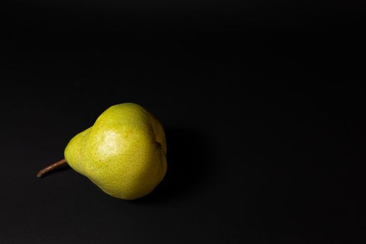 Ripe green pear on a dark background, late november pear variety. Whole fruit