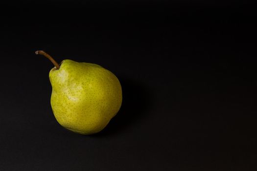 Ripe green pear on a dark background, late november pear variety. Whole fruit