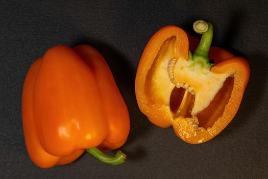 Two ripe orange bell peppers on a dark background, whole bell papper and cut in half