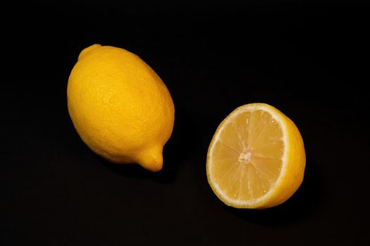 Two ripe lemons on a dark background, whole lemon and cut in half