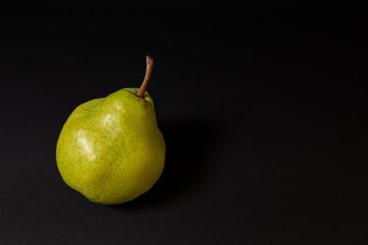 Ripe green pear on a dark background, late november pear variety. Whole fruit