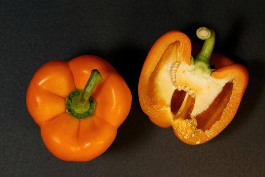 Two ripe orange bell peppers on a dark background, whole bell papper and cut in half