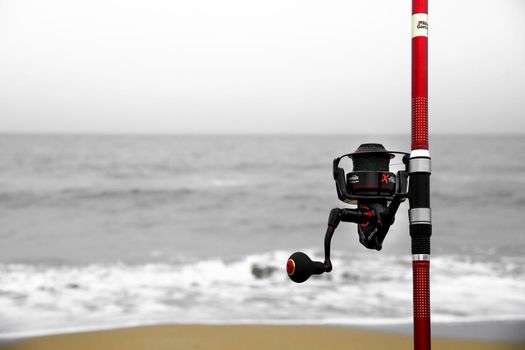 El Pinet, Alicante, Spain- March 30, 2022: Red Fishing rod on the shore on a cloudy day on El Pinet Beach in Alicante