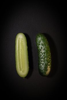 Two green cucumbers on a dark background. Whole cucumber and cut in half