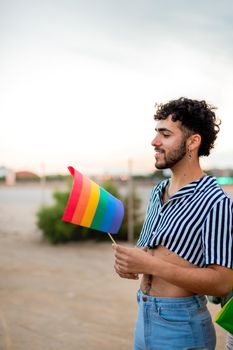 Vertical portrait of young gay man holding rainbow lgbt flag. Copy space. LGBT rights and tolerance concept.