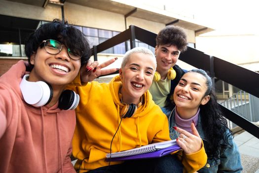 Multiracial group of college friends taking selfie with phone outside university building. Students laughing and having fun. Youth lifestyle concept.