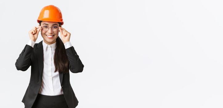 Smiling successful businesswoman in black suit and safety helmet visit construction area to monitor work, smiling satisfied, put on glasses, building engineer managing workers, white background.