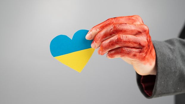 Woman with hands covered in blood holding a heart with the flag of ukraine on a white background