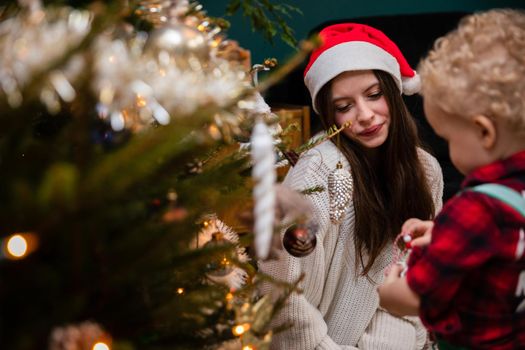 Siblings while decorating a Christmas tree. A two-year-old child with curly blonde hair and a teenage brunette as brother and sister.