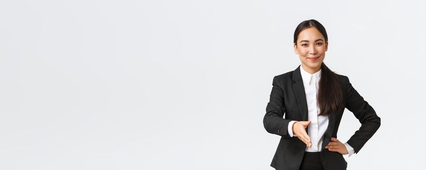 Confident successful businesswoman in black suit extend hand for handshake, greeting business partner with pleased determined smile, ready sign contract, white background.