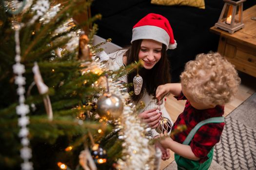 A teenage girl and her brother decorate a Christmas tree for Christmas. A two-year-old child with curly blonde hair.