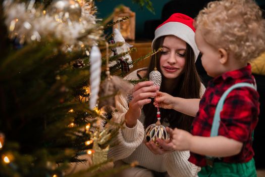 A teenage girl and her brother decorate a Christmas tree for Christmas. A two-year-old child with curly blonde hair.