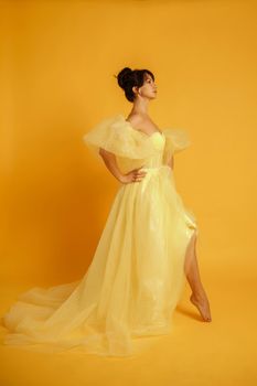 Profile portrait of a beautiful middle-aged woman in a yellow dress, her hair pulled up against a yellow background.