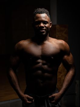 Portrait of an African American man with a naked torso in a dark studio. Muscular guy