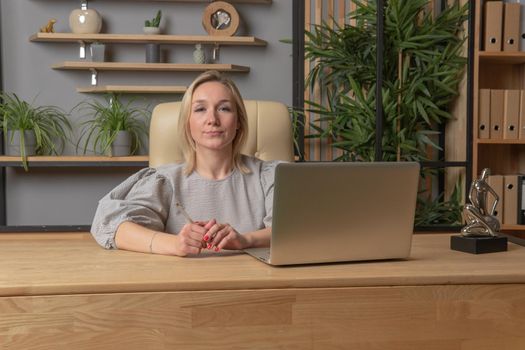 At a table with a laptop sits a girl in the hands of a pen business girl laptop woman work, for person female in online adult typing, student hispanic. Background indoors headphone, evening executive