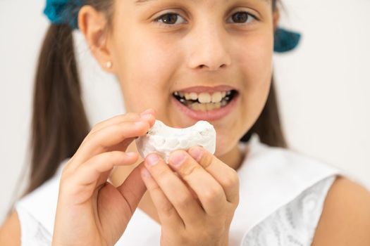 Teenager is holding a dental cast model at the start of orthodontic treatment alongside her teeth after the treatment was completed