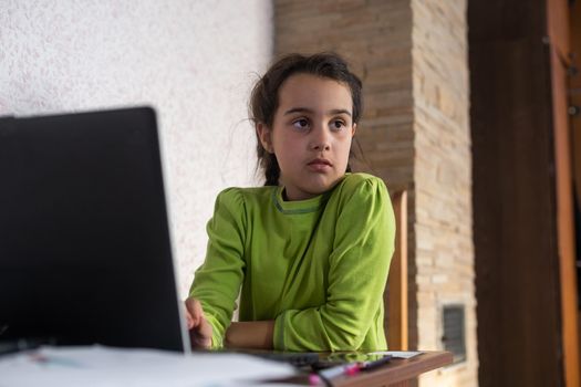 Child online. A little girl uses a laptop video chat to communicate learning while sitting at a table at home