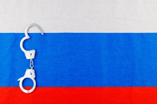 silver metal opened handcuffs laid on Russian flag full-frame background.