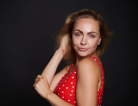 Attractive stunning middle aged blonde sporty woman with fresh clean tanned skin in red swimsuit with white polka dots confidently looking at camera isolated over black background with copy ad space
