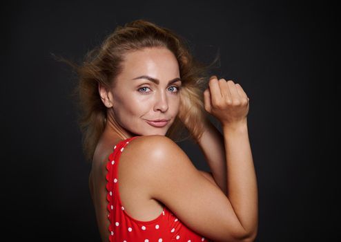 Portrait of a beautiful middle aged Caucasian woman with natural makeup and healthy glowing tanned skin, shiny flying blond hair, wearing red swimsuit isolated over black background with copy space