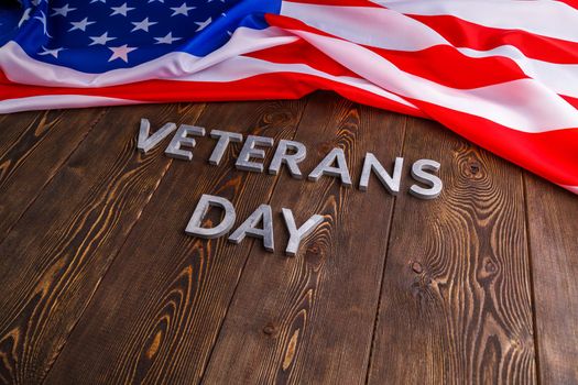 the words veterans day laid with silver metal letters on wooden board surface with crumpled usa flag.