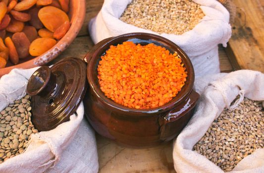 Ceramic clay pot with red lentils and sacks of legumes and grains in a food market stand