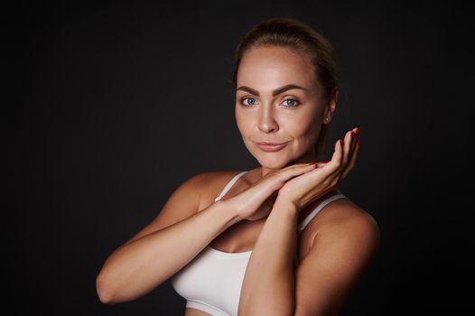 Attractive Caucasian middle aged pretty woman with perfect clean healthy skin and natural makeup confidently looking at camera, isolated over black background with copy space for advertisements