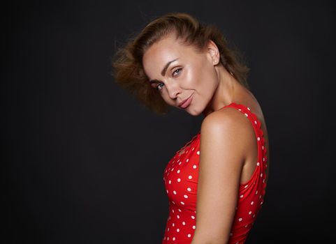 Side beauty shot portrait charming stunning blonde pretty woman with beautiful healthy skin and flat belly wearing red swimsuit with white polka dots posing against black background with copy ad space